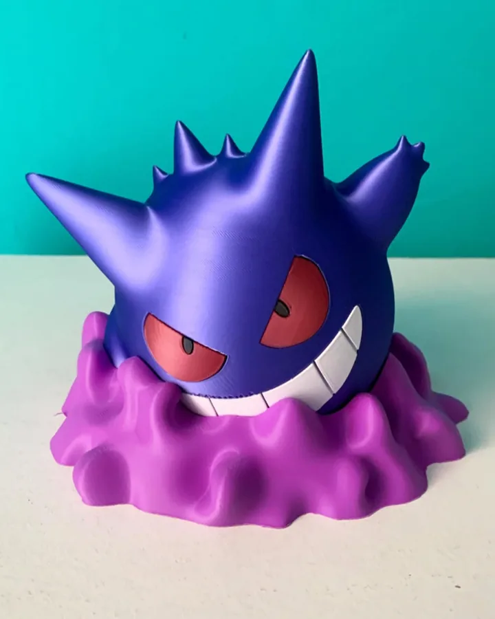 Peça de Gengar impressa em 3D em roxo e azul sobre base de névoa em lilás